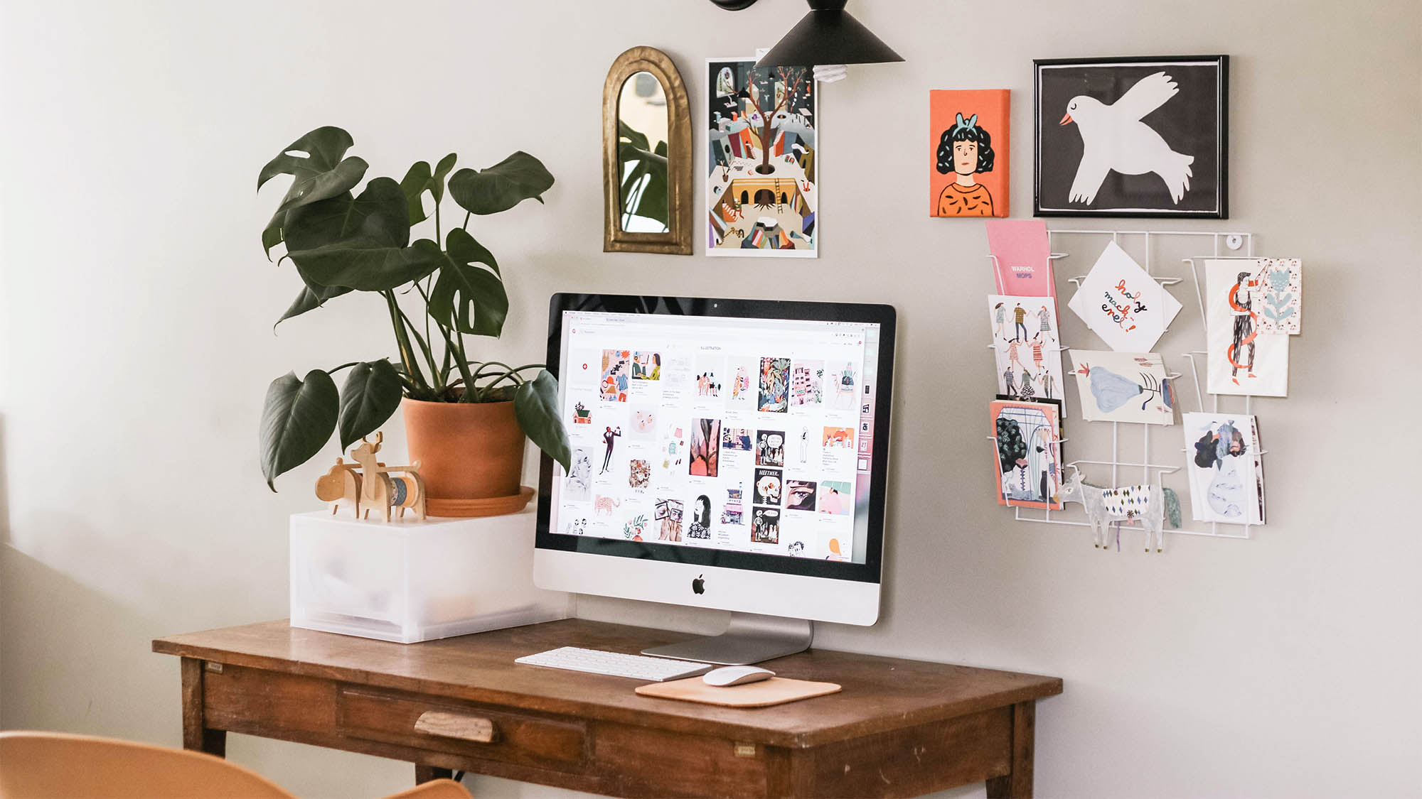 Wood desk with Mac monitor, houseplant and colorful wall art in background
