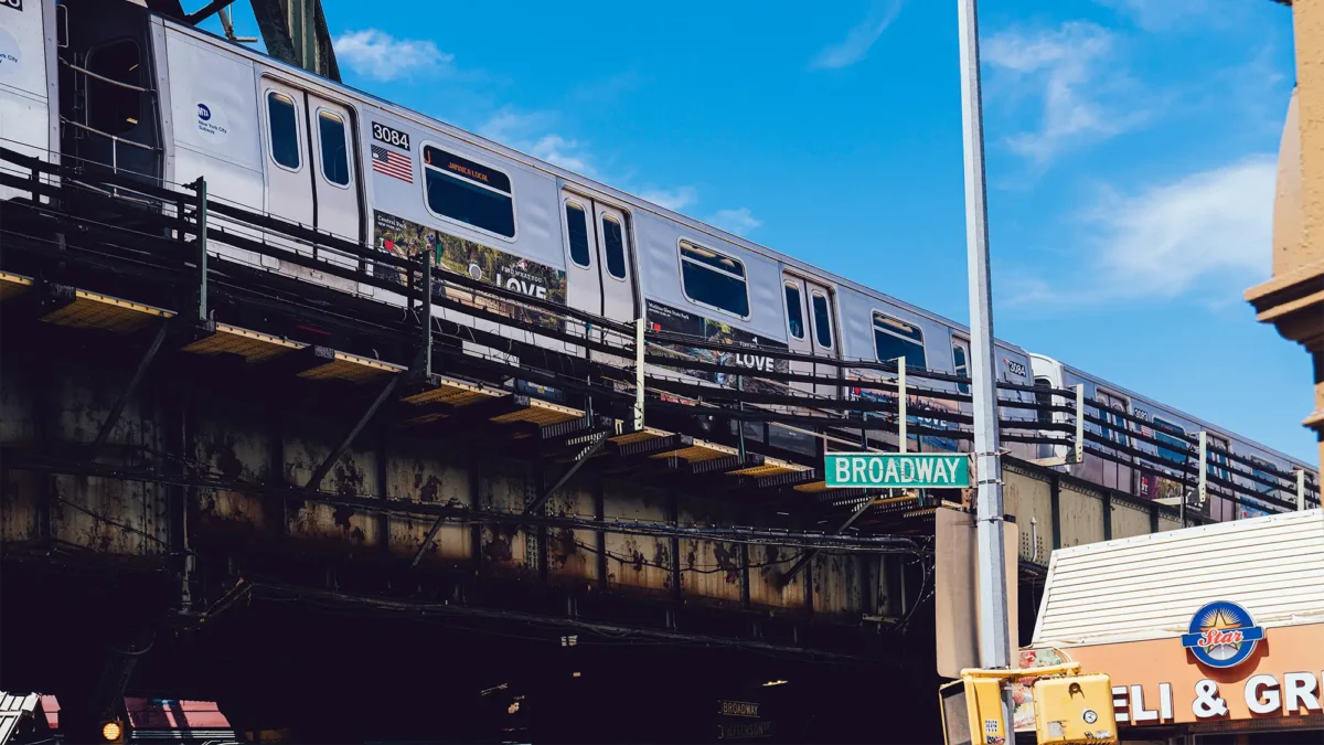 NYC subway on elevated track passing by Broadway street sign