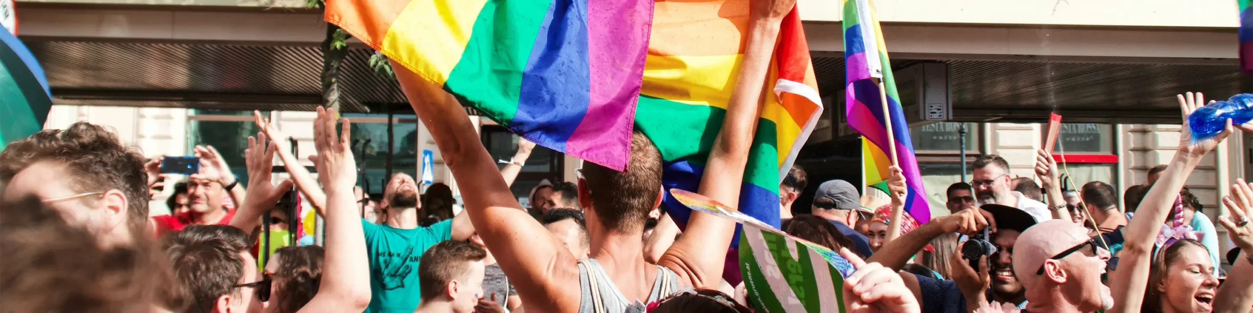 People waving rainbow Pride flags at outdoor city parade