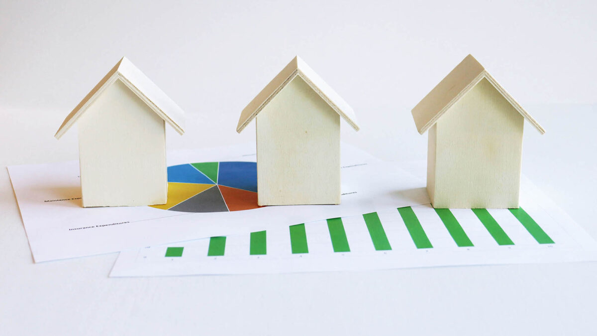 Three wooden houses on top of paper with pie chart and bar graph