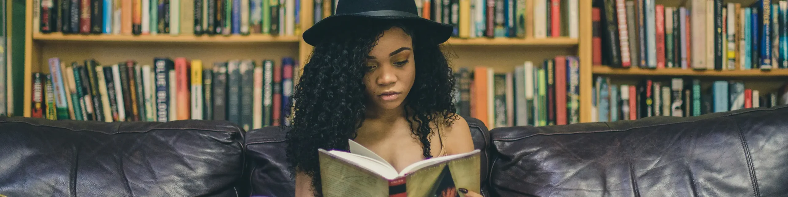 Black woman sitting in front of bookshelf reading book